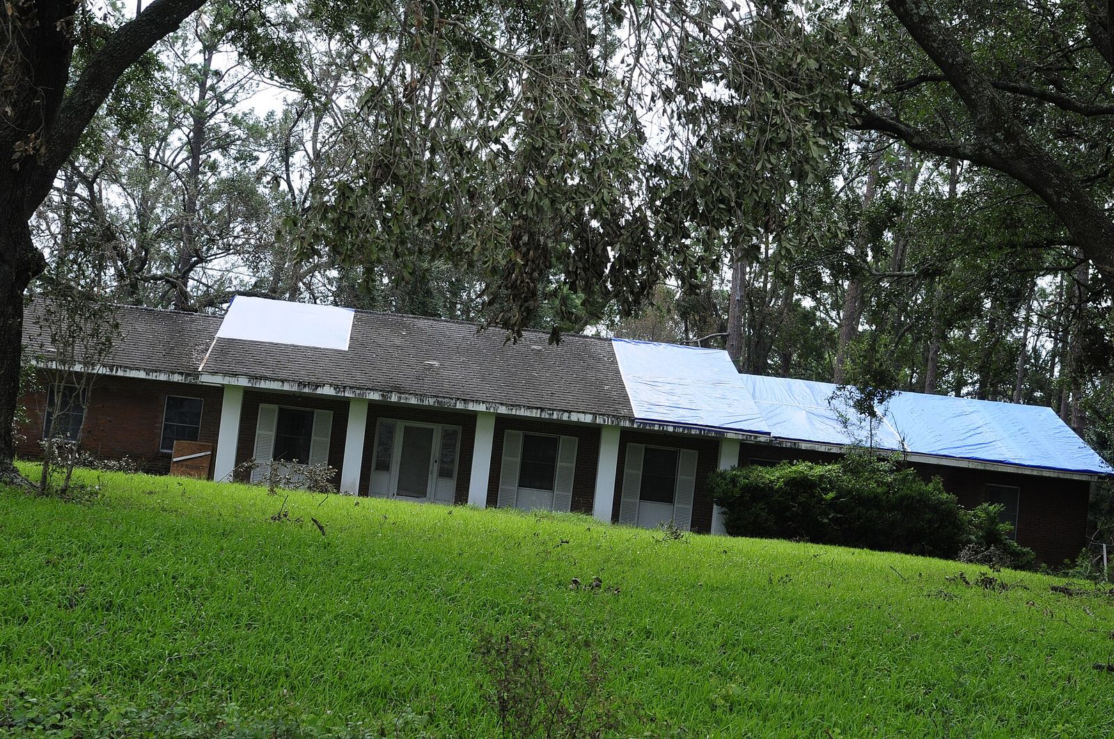Ranch house with a blue tarp covering the damaged half of its roof after a storm