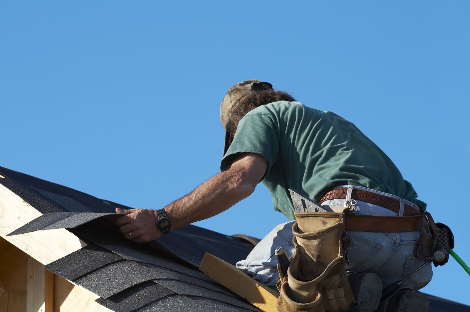 Roofer kneeling at the eave of a house, fitting the first course of shingles