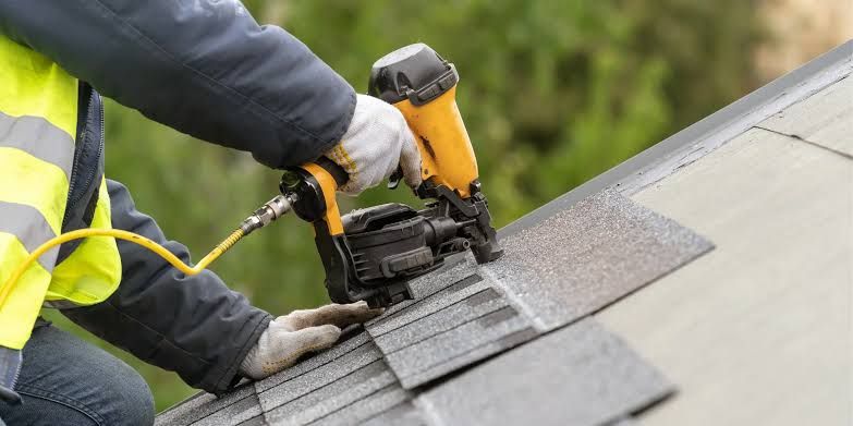 Close view of a roofer nailing an architectural shingle with a coil nailer